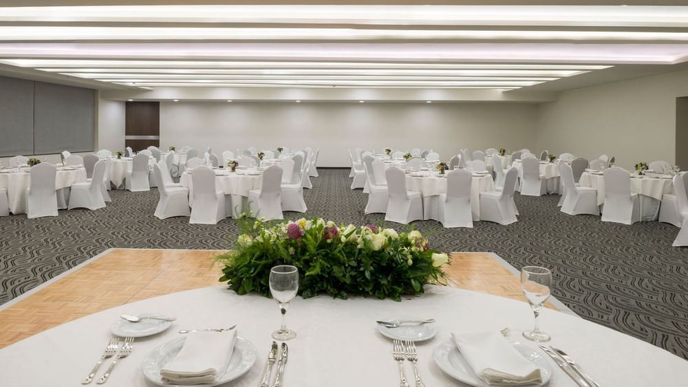 CDMX ballroom set for a banquet with white linens and floral centerpieces on tables at Real Inn Celaya