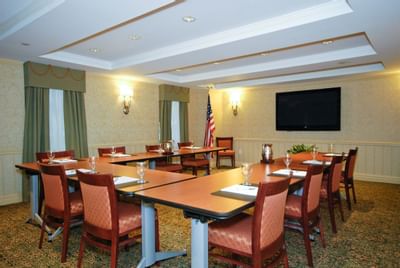 Valencia Conference room with long tables, chairs, wine glasses, TV, flag, and windows with green drapes.