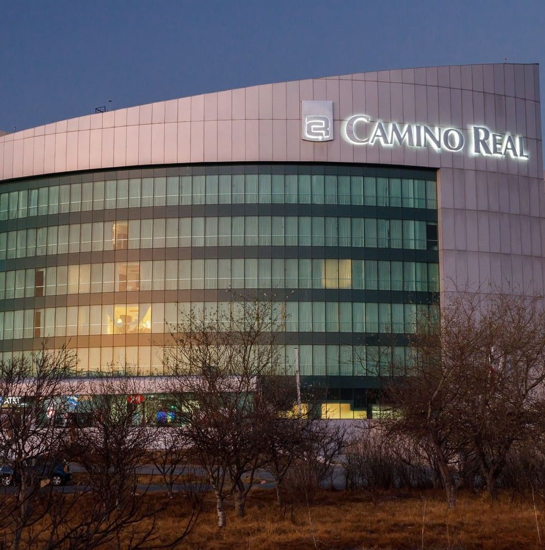 Exterior view of curved Camino Real Pachuca building at dusk, featuring glowing windows and signage