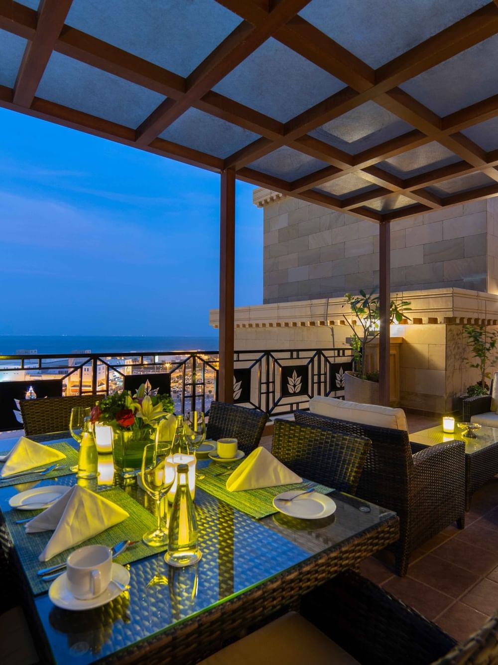 Outdoor dining set under a lit wooden pergola overlooking the city lights in Penthouse Villa at dusk at Warwick Al Khobar