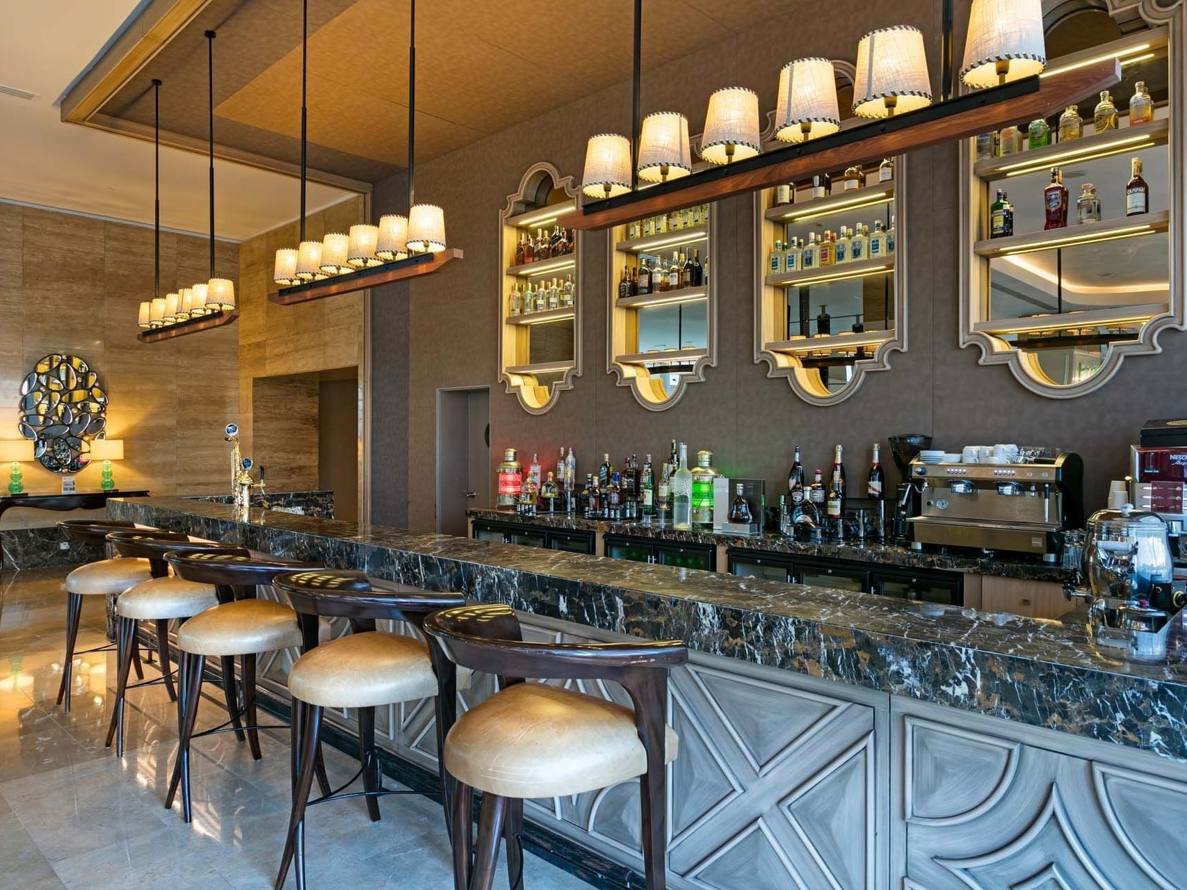 Cordelia Lobby Bar with stools, hanging lights, and shelves of liquor and glasses at Titanic Deluxe Lara