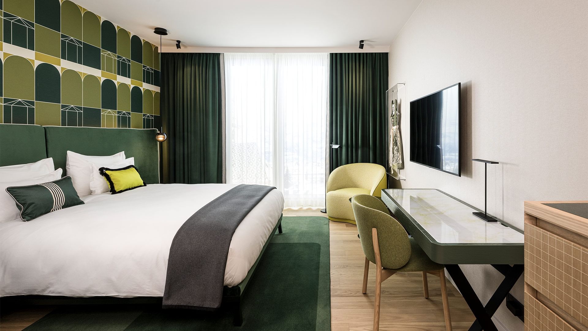 Zimmer mit Bett, grünem Teppich, Schreibtisch, Stuhl, Fernseher und gelbem Sessel.