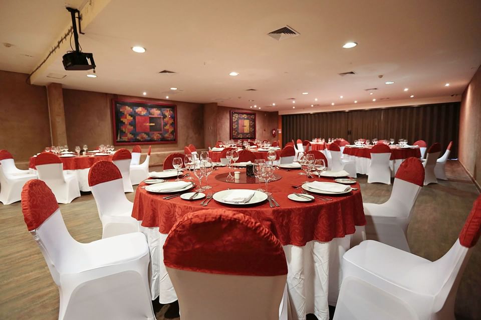 Sala de banquetes con mesas cubiertas de rojo y sillas blancas en Cumbres San Pedro