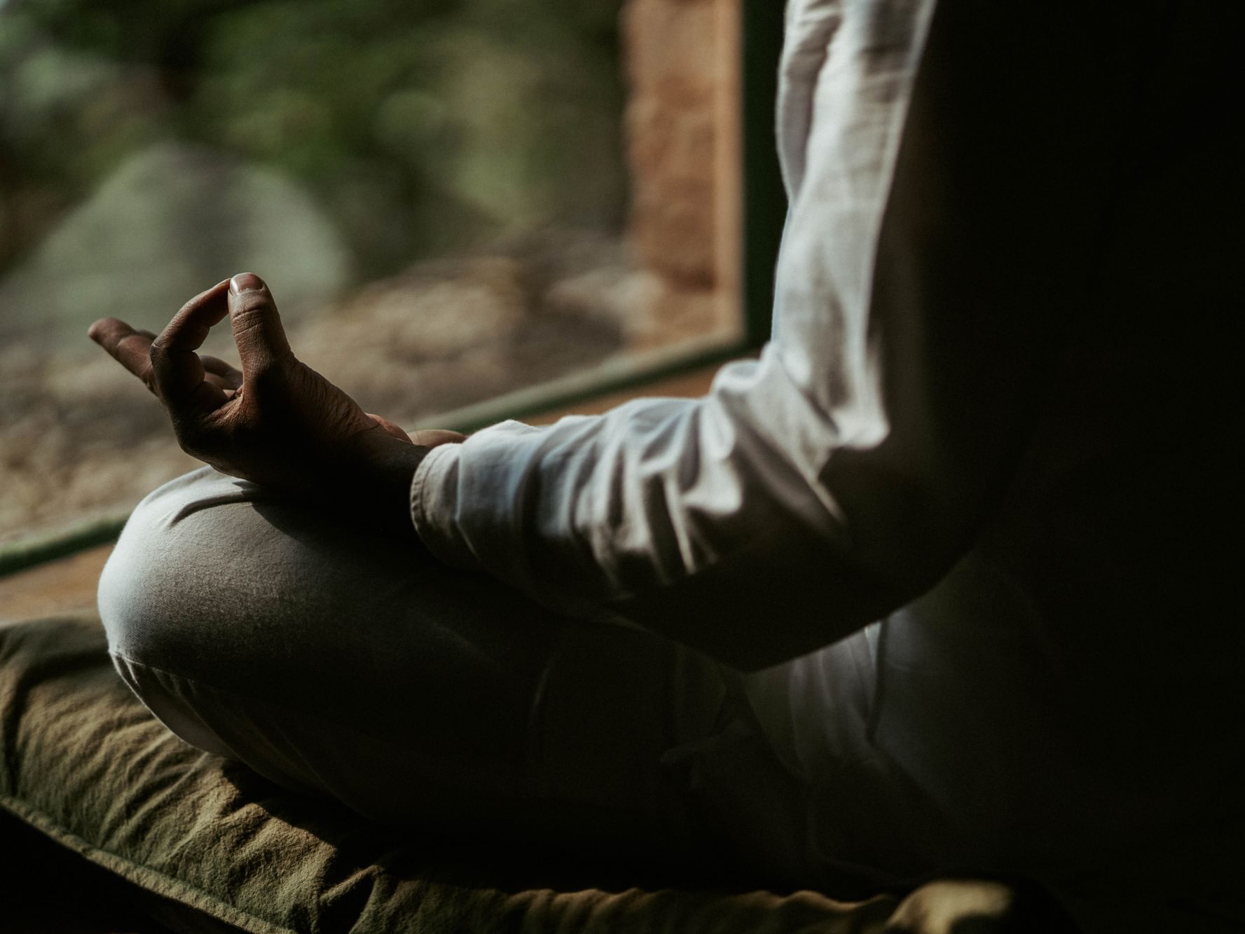 Close-up of a person's hand in a meditative pose, sitting cross-legged by a window at Dwarika's Himalayan Wellbeing