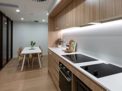 Modern kitchen with wooden cabinets, white countertop, induction cooktop, and dining area at UniLodge Brisbane City.