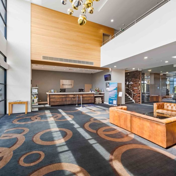 Lobby with wooden reception desk, leather sofas, patterned carpet, and a staircase at Mercure Kooindah Waters