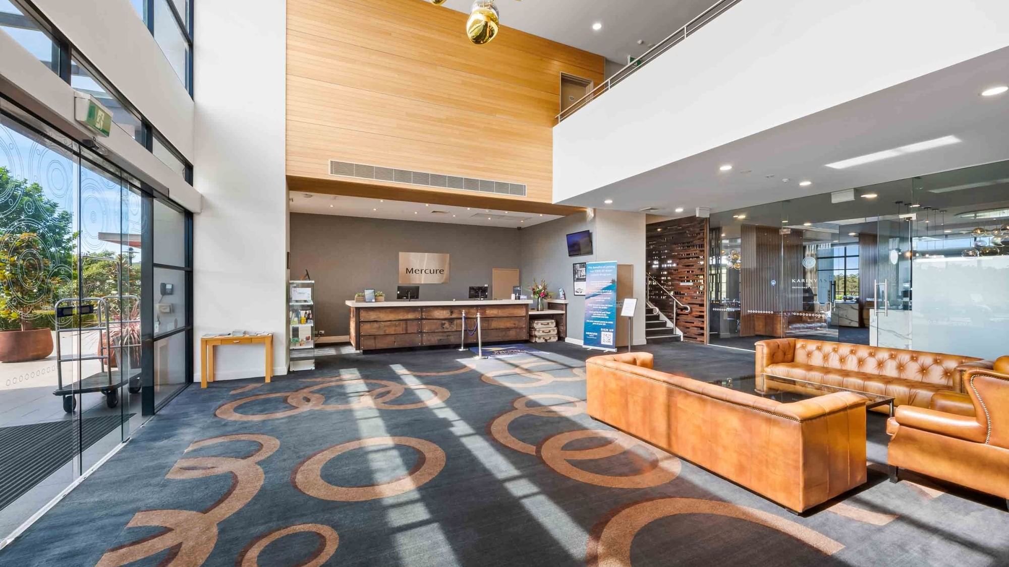 Lobby with wooden reception desk, leather sofas, patterned carpet, and a staircase at Mercure Kooindah Waters