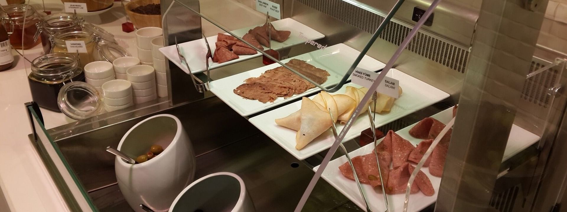 Breakfast & In-Room Dining  with Sliced meats on plates by olives in white bowls under a glass protector at Warwick Ankara