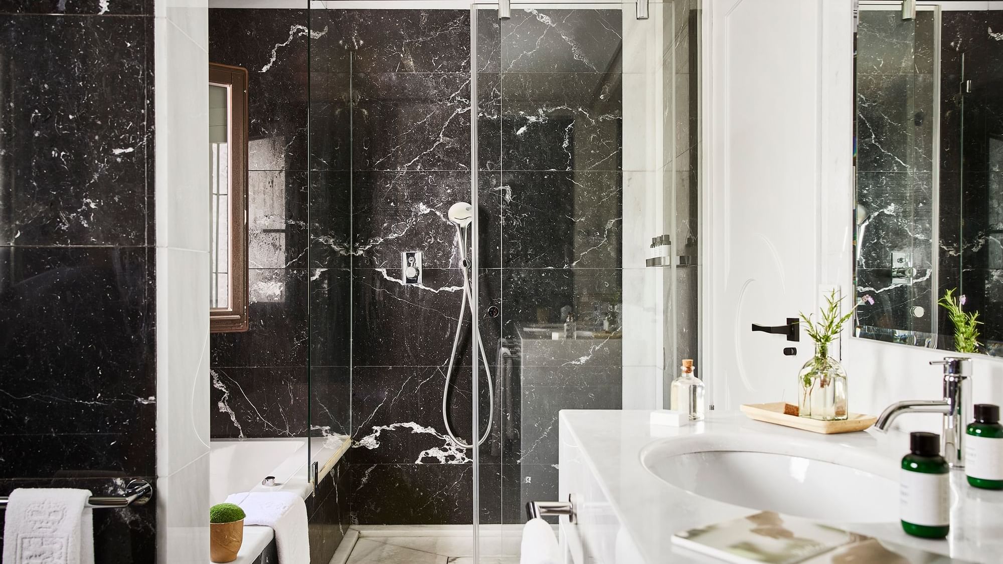 Santa Margarita Two-Bedroom Suite bathroom with black marble walls and a glass shower beside the sink at Marbella Club