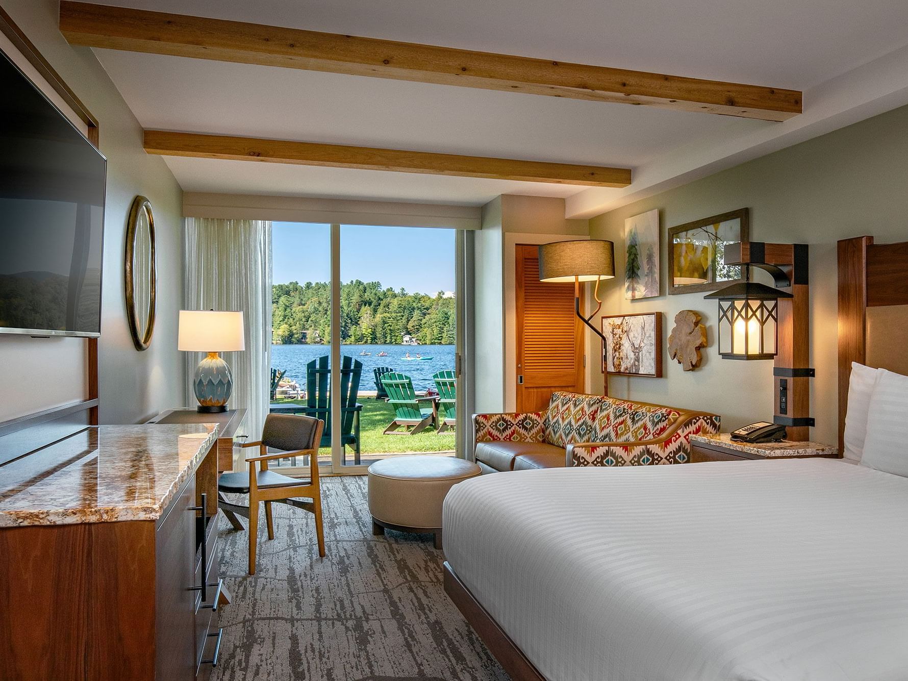 TV facing bed with a paterened sofa by the window and a work desk in Lake View King at High Peaks Resort
