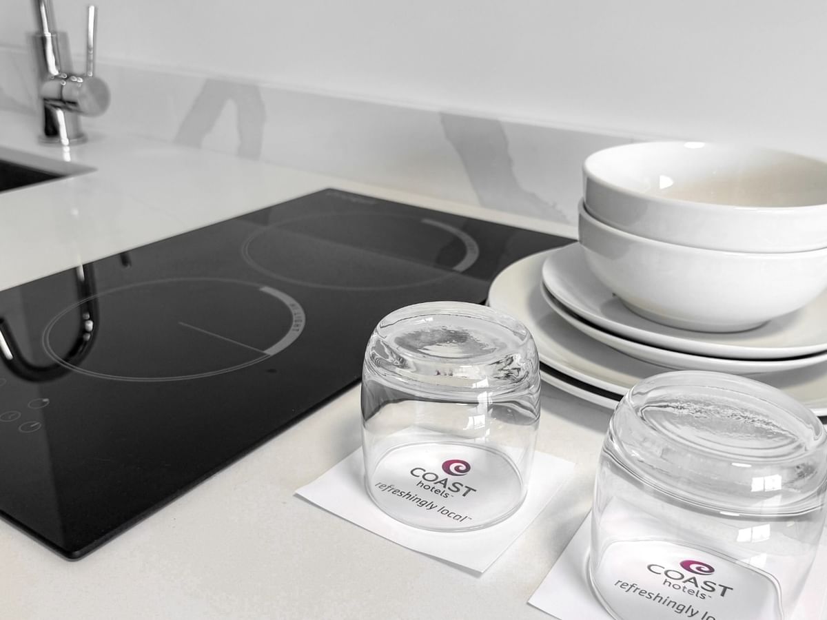 A kitchenette with stacked white bowls and plates, glasses, and sink.