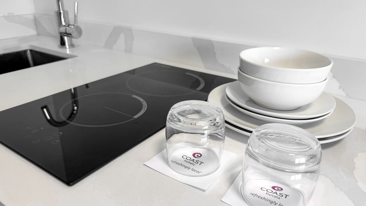 A kitchenette with stacked white bowls and plates, glasses, and sink.