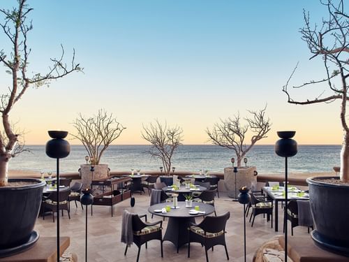 Patio al aire libre de De Cortez Grill House con mesas y sillas de mimbre, con vista al mar en Hacienda Del Mar Los Cabos