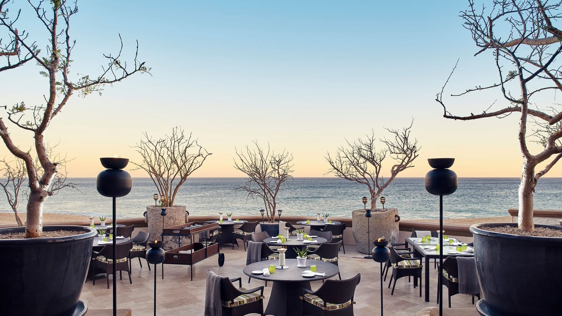 Patio al aire libre de De Cortez Grill House con mesas y sillas de mimbre, con vista al mar en Hacienda Del Mar Los Cabos