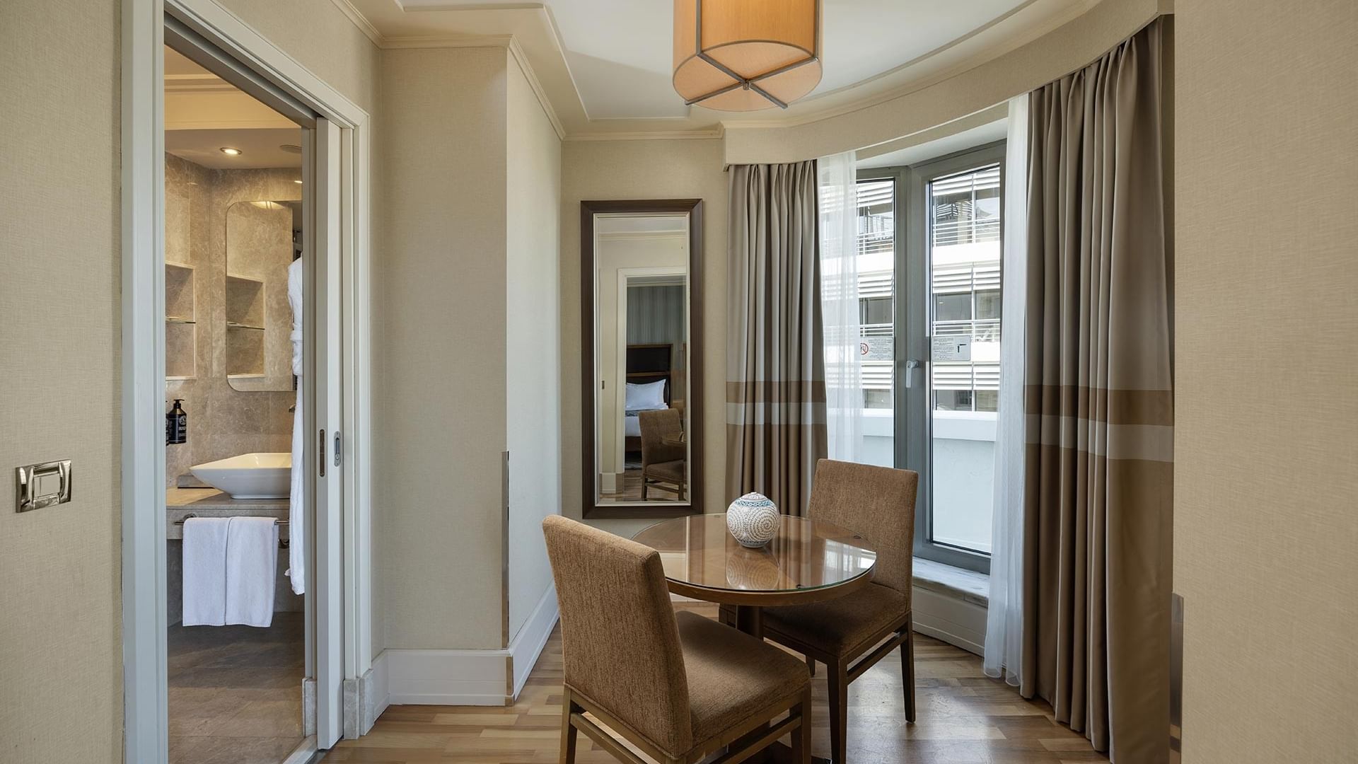Titanic City Taksim'deki deluxe odanın iç görünümü, masa ve sandalyeler, banyo ve pencere.