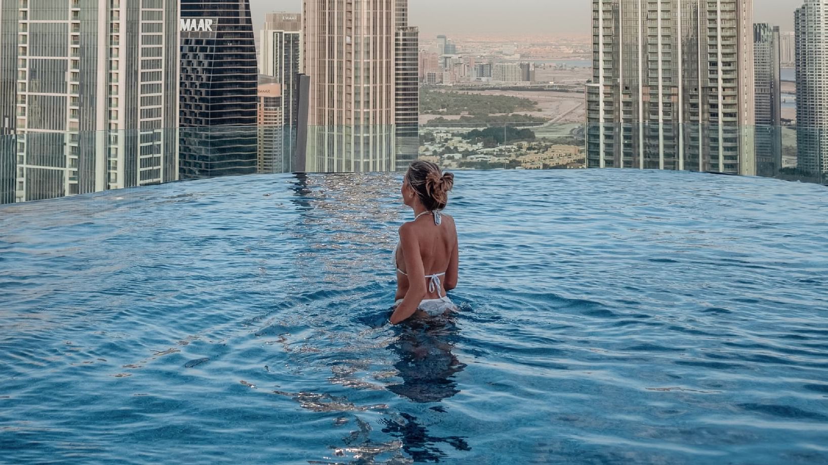 Woman stands in an infinity pool, overlooking a skyline of tall buildings and a distant horizon at Paramount Hotels