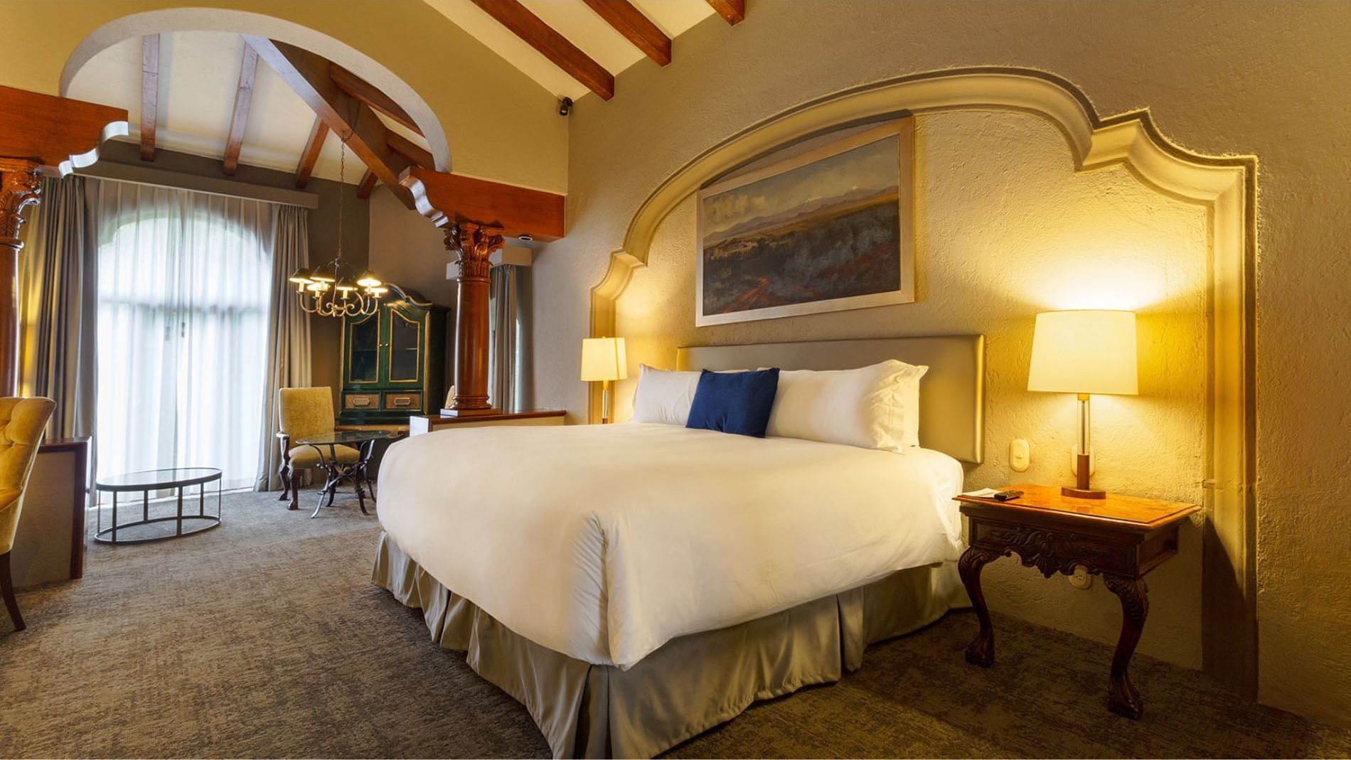 King Grand Class suite with exposed ceiling beams, an ornate headboard, and wood pillars at Quinta Real Guadalajara