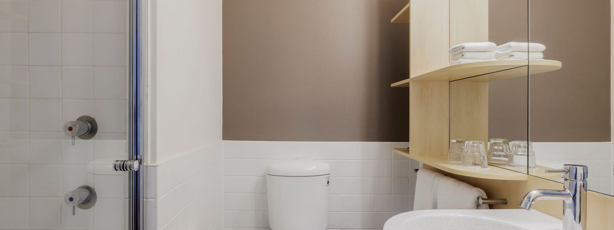 Shower area and wooden shelves with towels and glasses in Standard Room Queen Bed's bathroom at Novotel Sydney Olympic Park