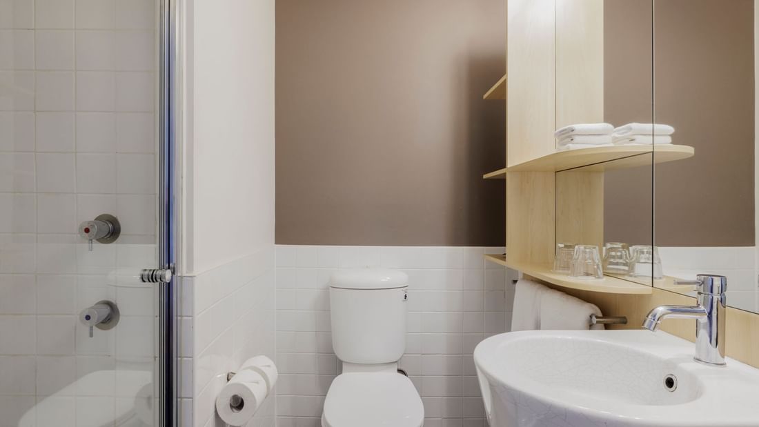 Shower area and wooden shelves with towels and glasses in Standard Room Queen Bed's bathroom at Novotel Sydney Olympic Park