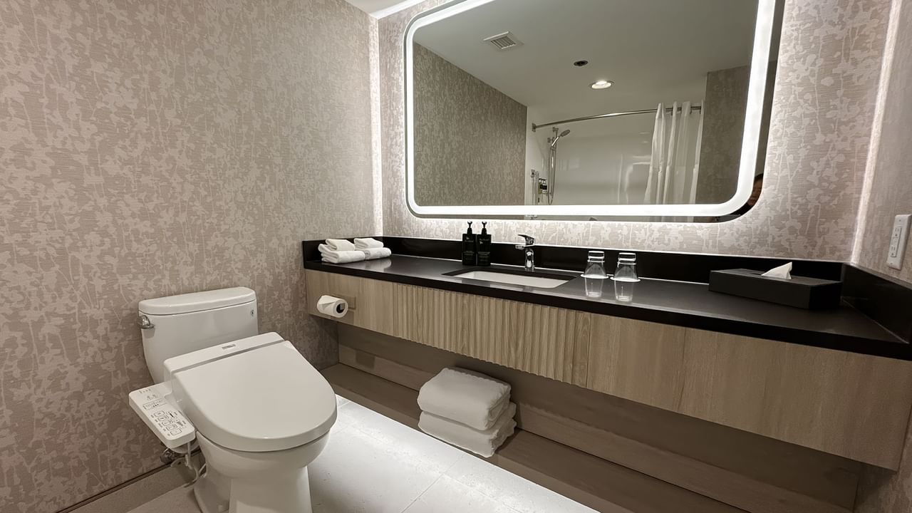 Hotel bathroom with toilet, mirror, sink, soap and towels