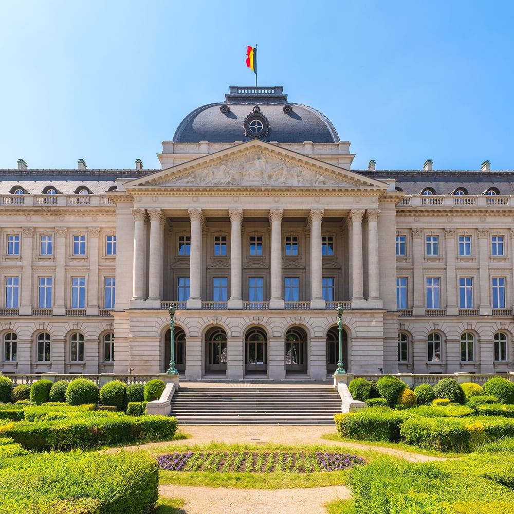 Grand facade of the Royal Palace, with flags flying, surrounded by manicured gardens near Warwick Grand Place Brussels