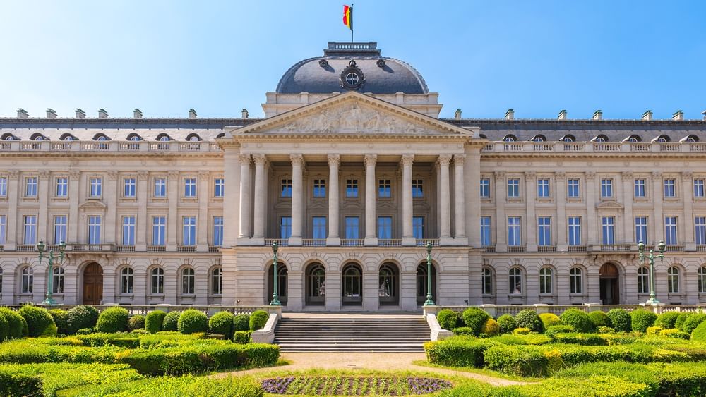 Grand facade of the Royal Palace, with flags flying, surrounded by manicured gardens near Warwick Grand Place Brussels
