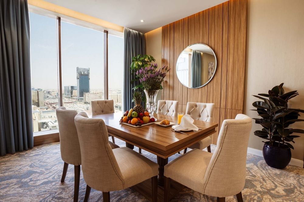 Royal Suite features Wooden dining table with chairs by a window under a round mirror at Cantonal Hotel by Warwick Riyadh
