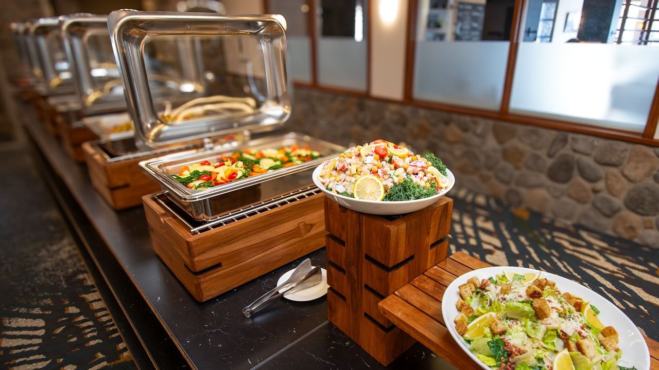Buffet line with dishes, trays, and assorted salads on plates.