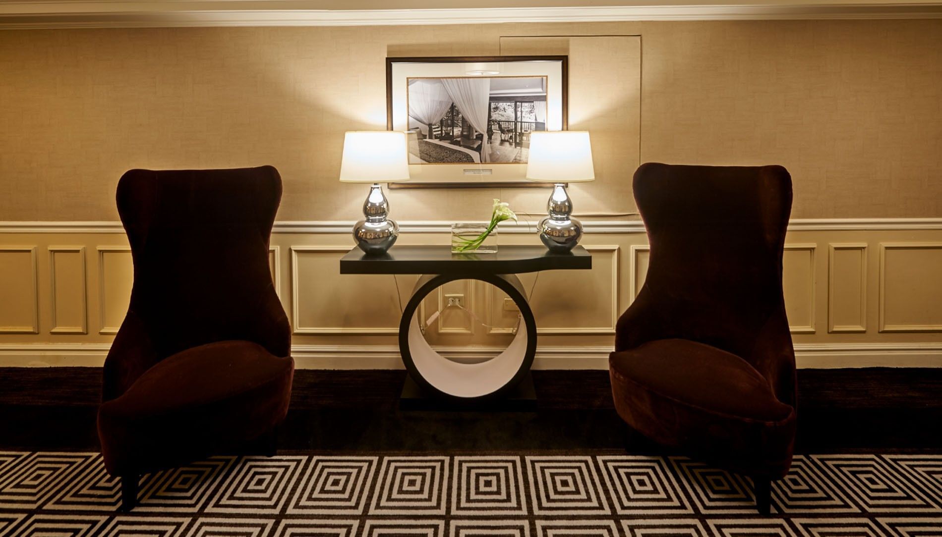 Two velvet wingback chairs by an ornate console table under a framed picture and lamps at Warwick Denver