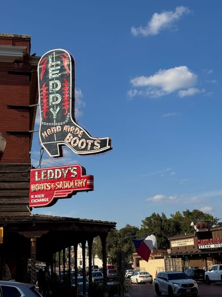 Neon boot sign by a brick building under a blue sky near the entrance at Warwick Melrose Dallas Hotel