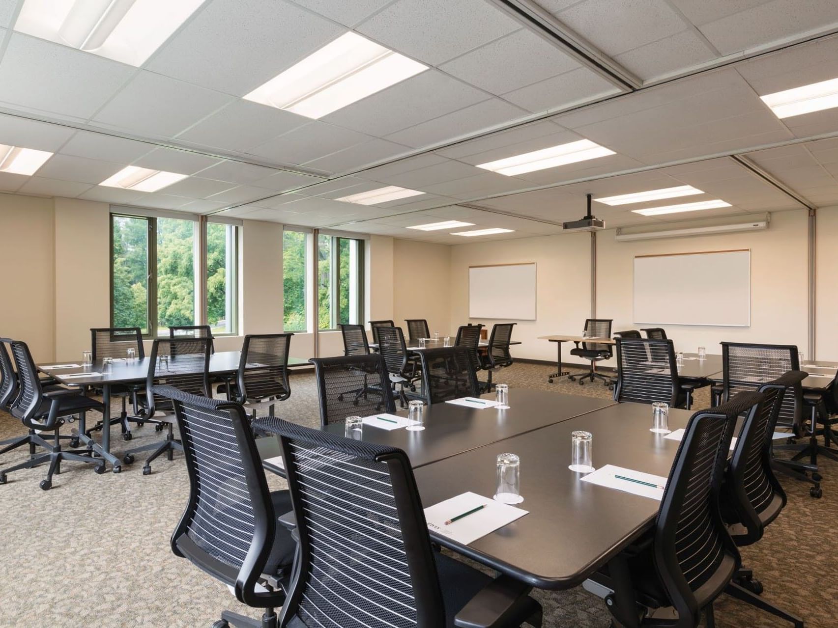 Black mesh rolling chairs around dark conference tables under bright panel lights in Juniper Room at Spencer Hotel