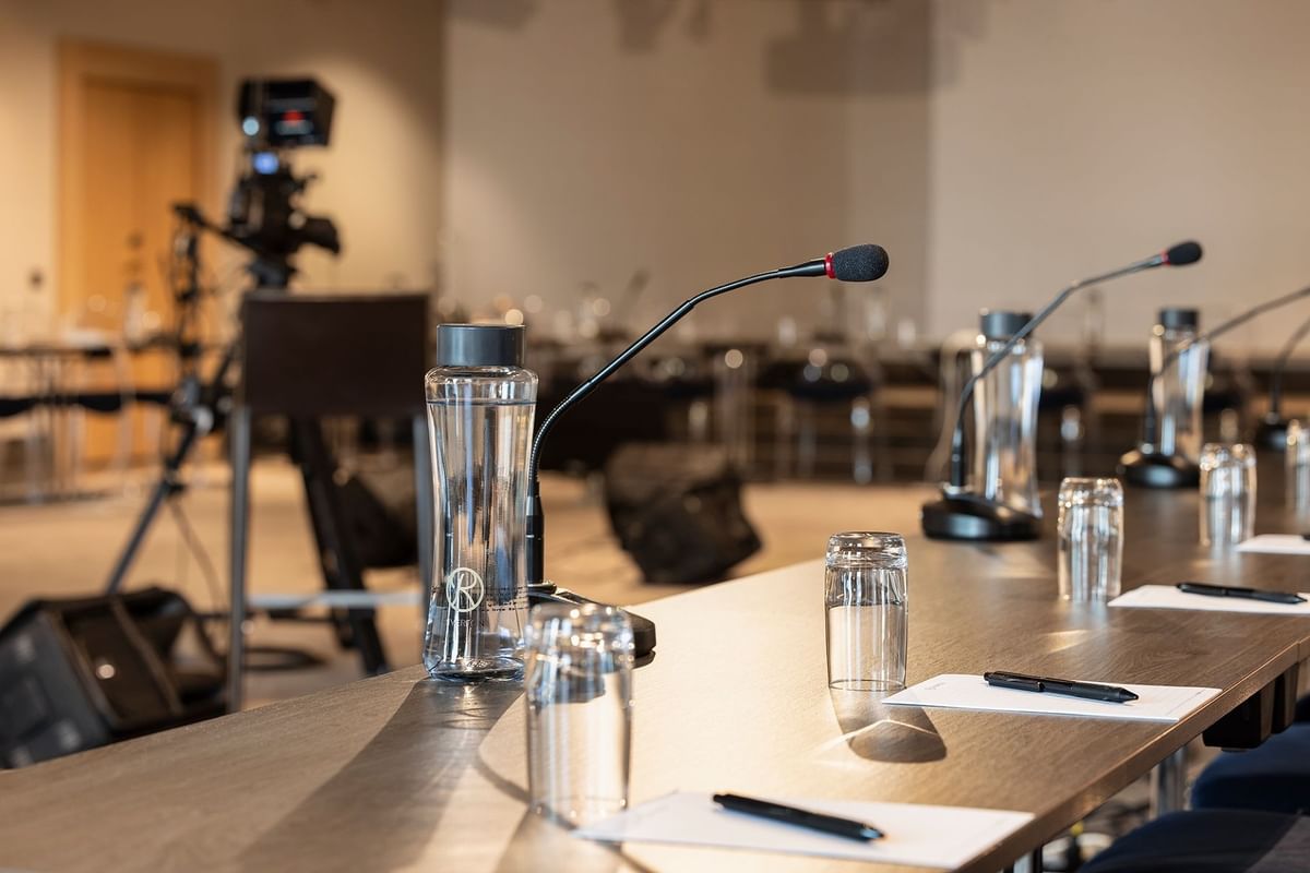 Konferensbord med mikrofoner, vattenglas och anteckningsblock i ett konferensrum.