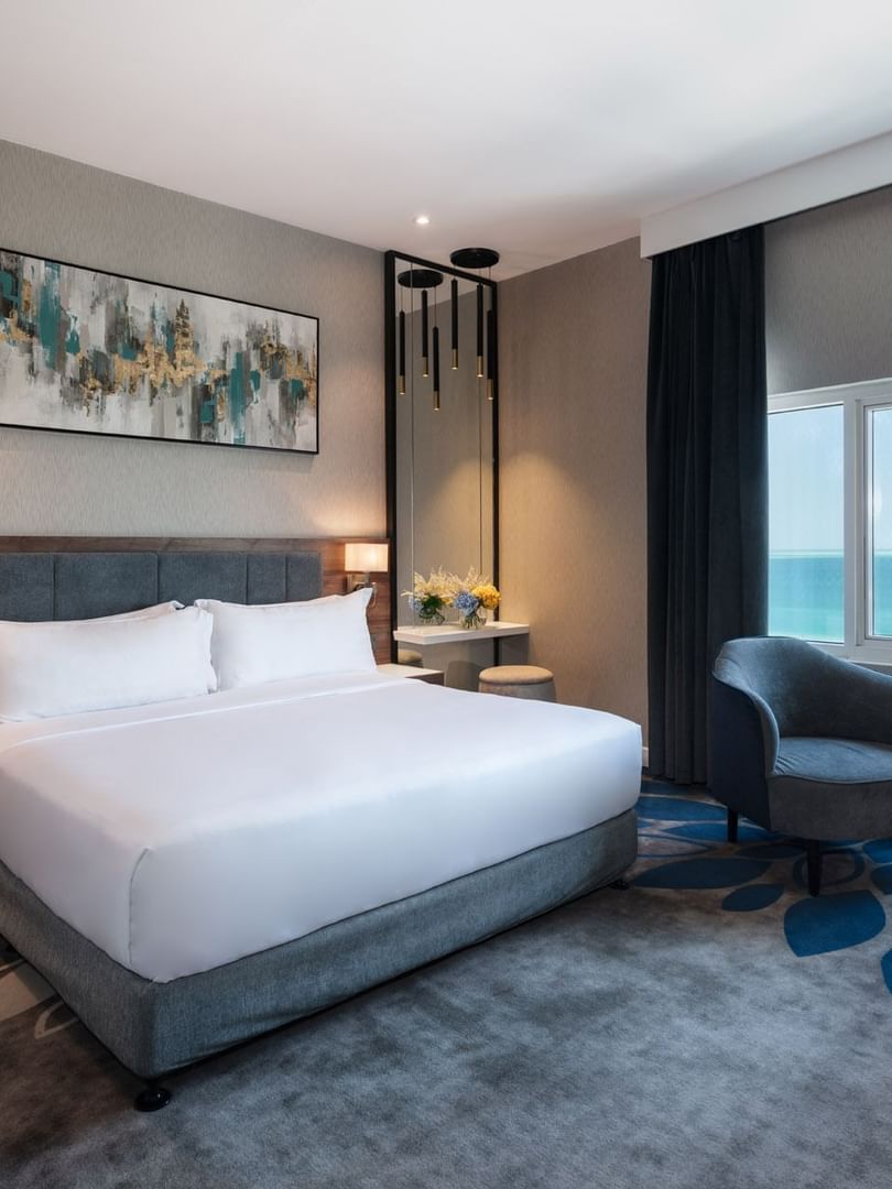 Dark armchair and small table near a large window overlooking a vast blue ocean in Standard Room at Warwick Al Jubail