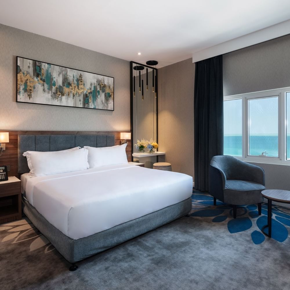 Dark armchair and small table near a large window overlooking a vast blue ocean in Standard Room at Warwick Al Jubail