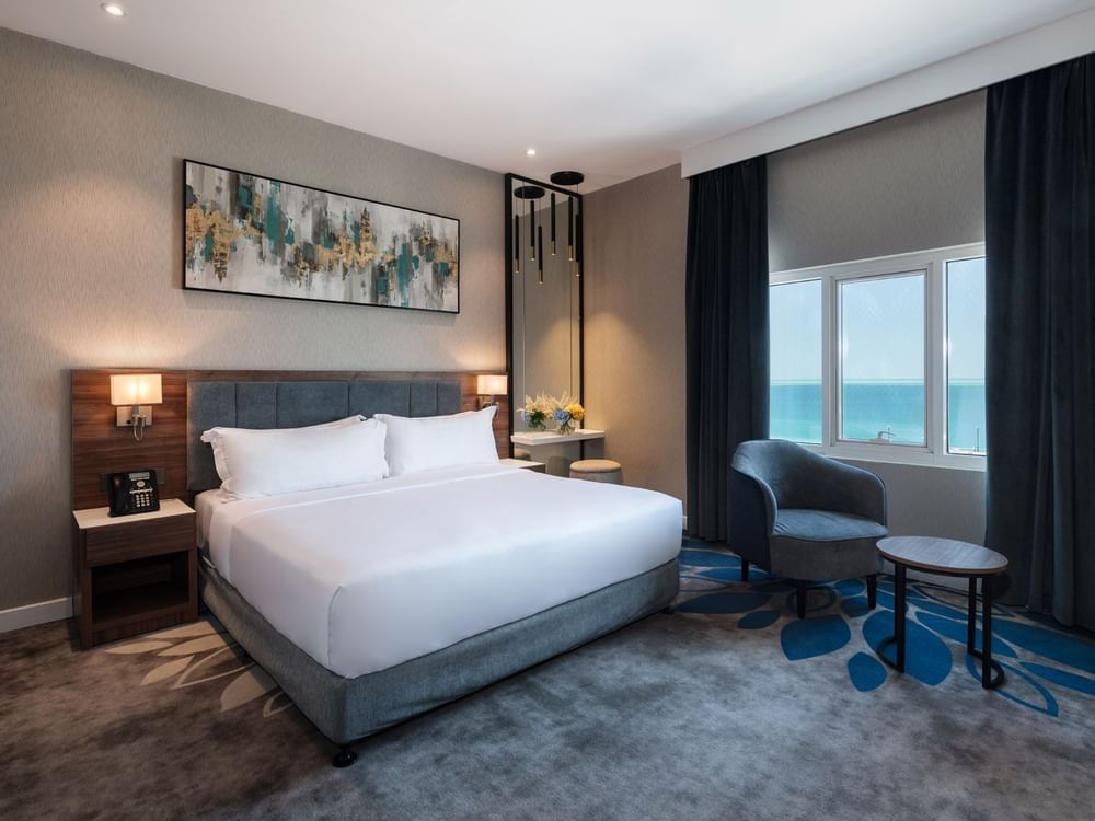 Dark armchair and small table near a large window overlooking a vast blue ocean in Standard Room at Warwick Al Jubail