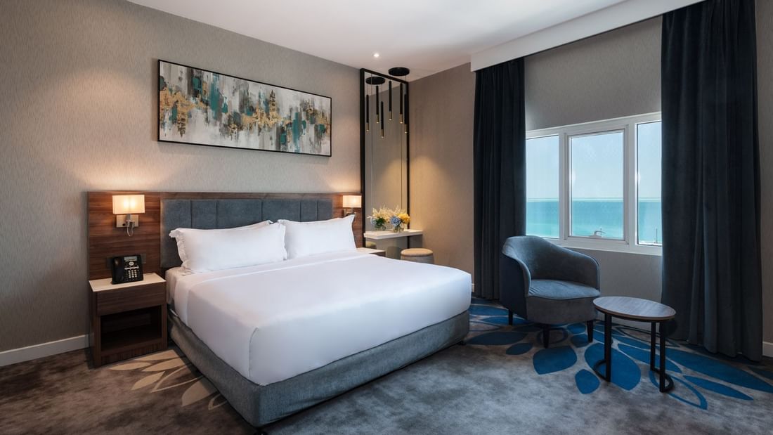 Dark armchair and small table near a large window overlooking a vast blue ocean in Standard Room at Warwick Al Jubail