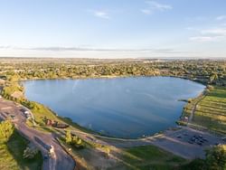 Aerial view of a serene blue lake surrounded by green spaces and parking areas at Lake Elmo State Park