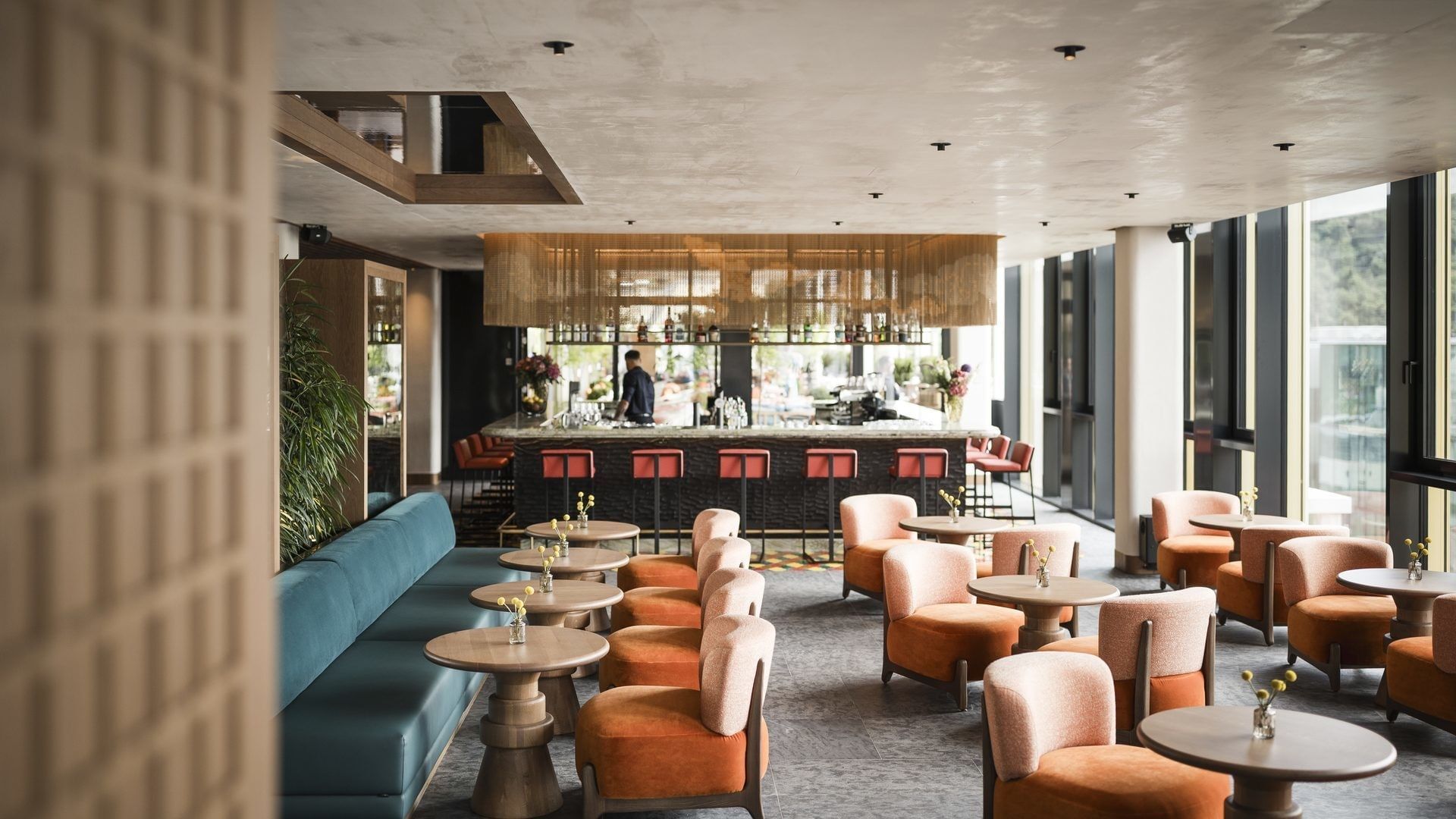 Lounge mit orangen Sesseln, runden Tischen und einer langen Theke im Hintergrund.