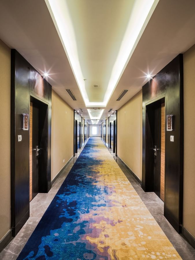Hallway with a blue and yellow carpet lined with dark wood doors leading to the Executive Suite at Naviti by Warwick Dammam