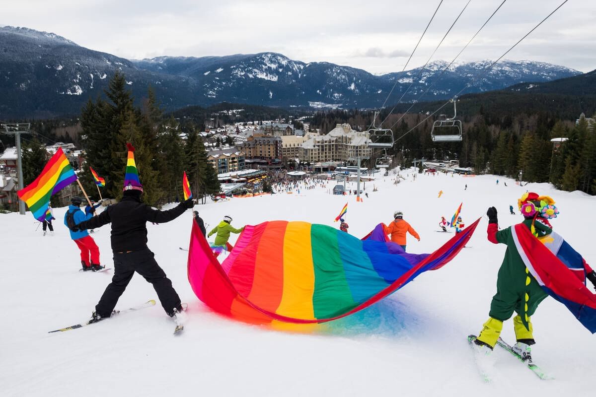 People skiing with a rainbow flag in the Whistler Pride and Ski Festival near Blackcomb Springs Suites