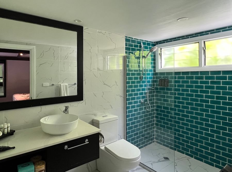 A bathroom with white sink and toilet, teal shower, and black framed mirror at Tambua Sands Beach Resort.