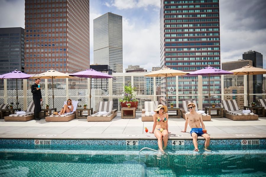 Guests sitting by a rooftop pool under umbrellas with city views at dusk at Warwick Denver