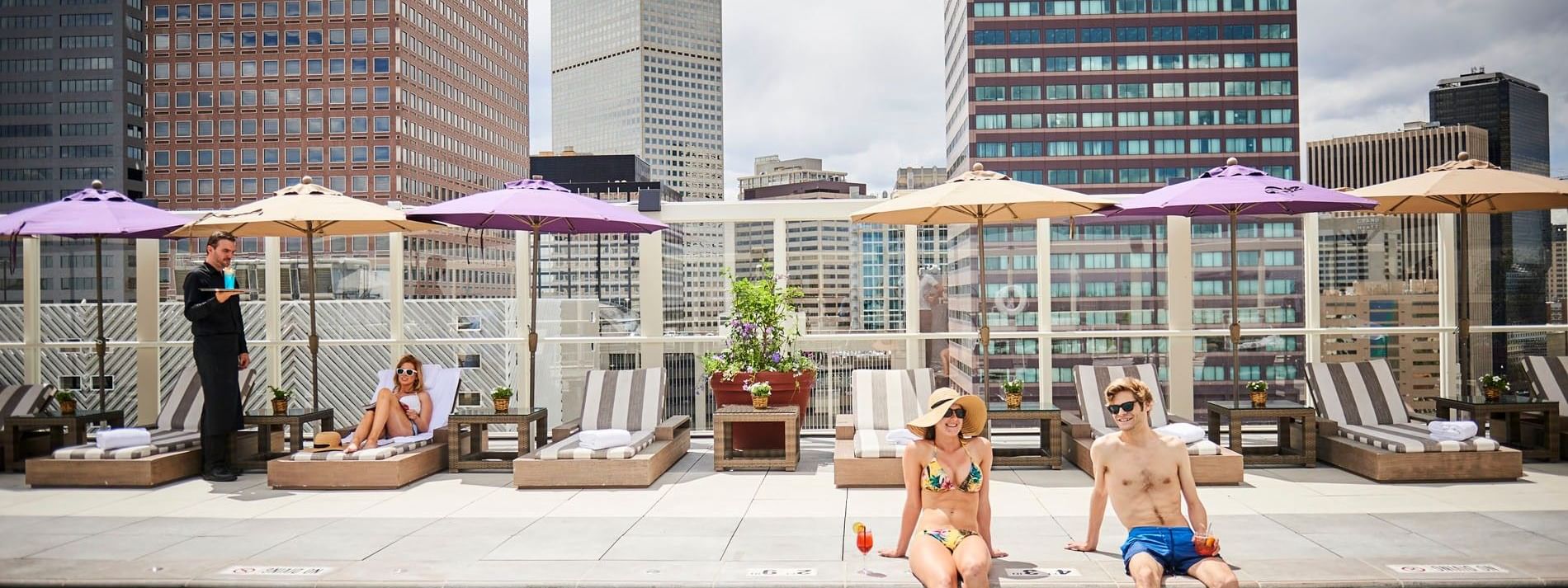Guests sitting by a rooftop pool under umbrellas with city views at dusk at Warwick Denver