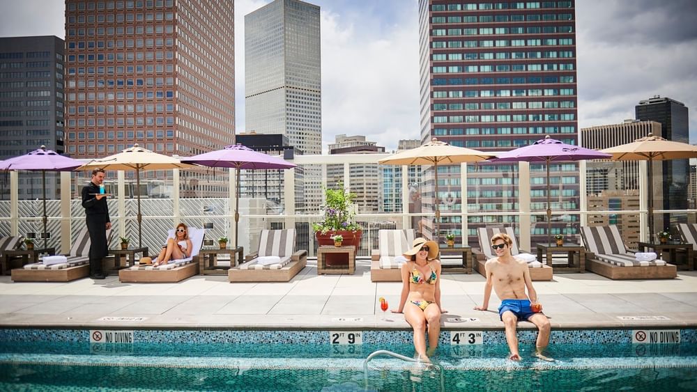 Guests sitting by a rooftop pool under umbrellas with city views at dusk at Warwick Denver