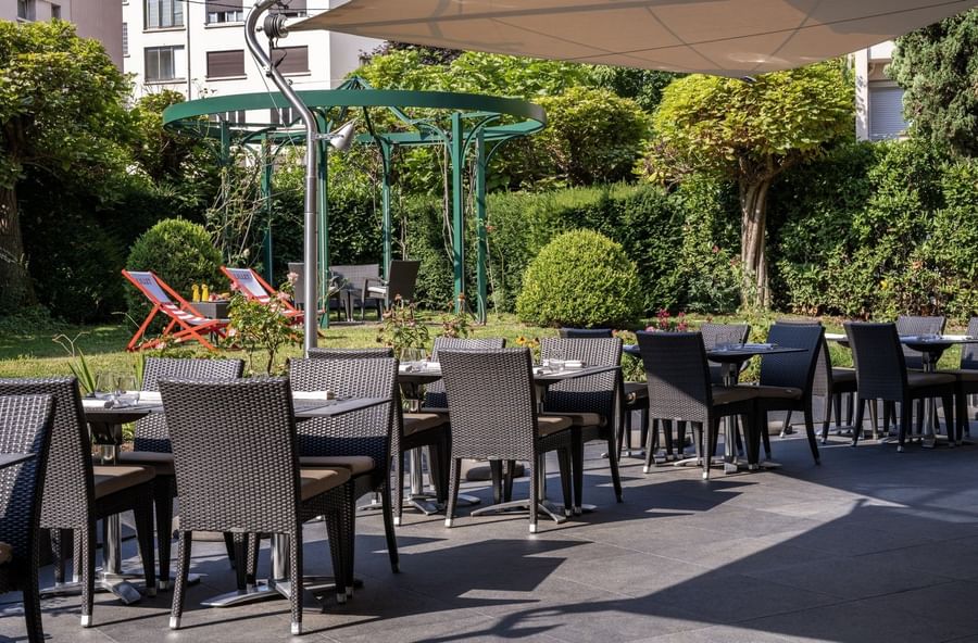 Outdoor patio of Le Lounge Restaurant with wicker chairs and tables, shaded by modern awnings at Warwick Reine Astrid - Lyon