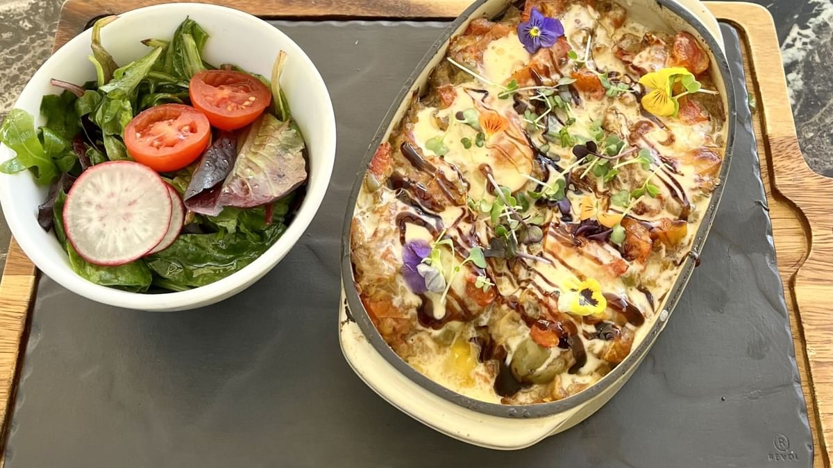 Salade de légumes et plat gratiné avec sauce et fleurs comestibles sur une planche en bois.