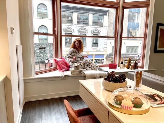 A lady in cozy loungewear sits by a large window, surrounded by festive decorations at ReStays Ottawa