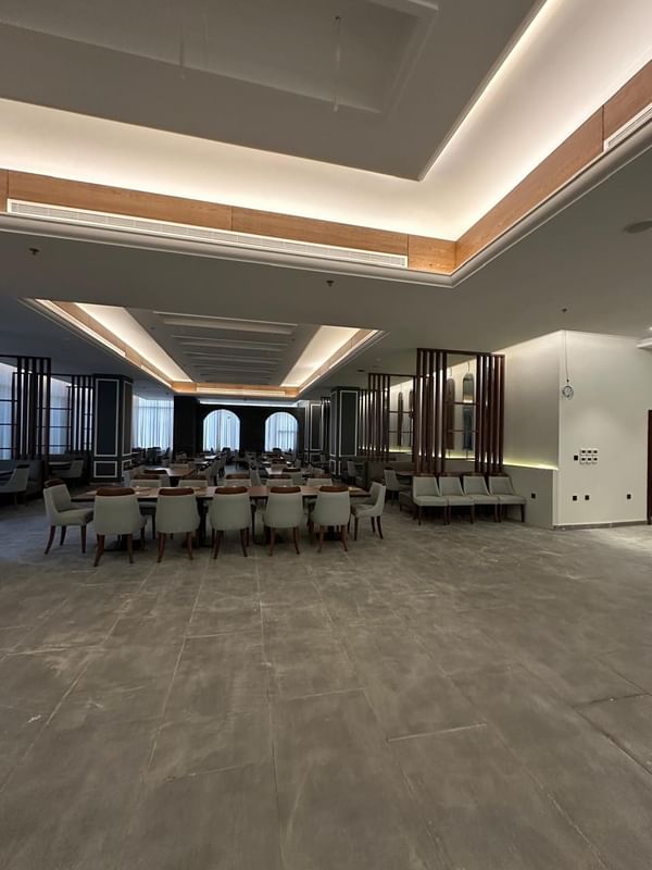 Almir Restaurant dining area with gray chairs by long wooden tables at Warwick Jeddah Hotel & Spa