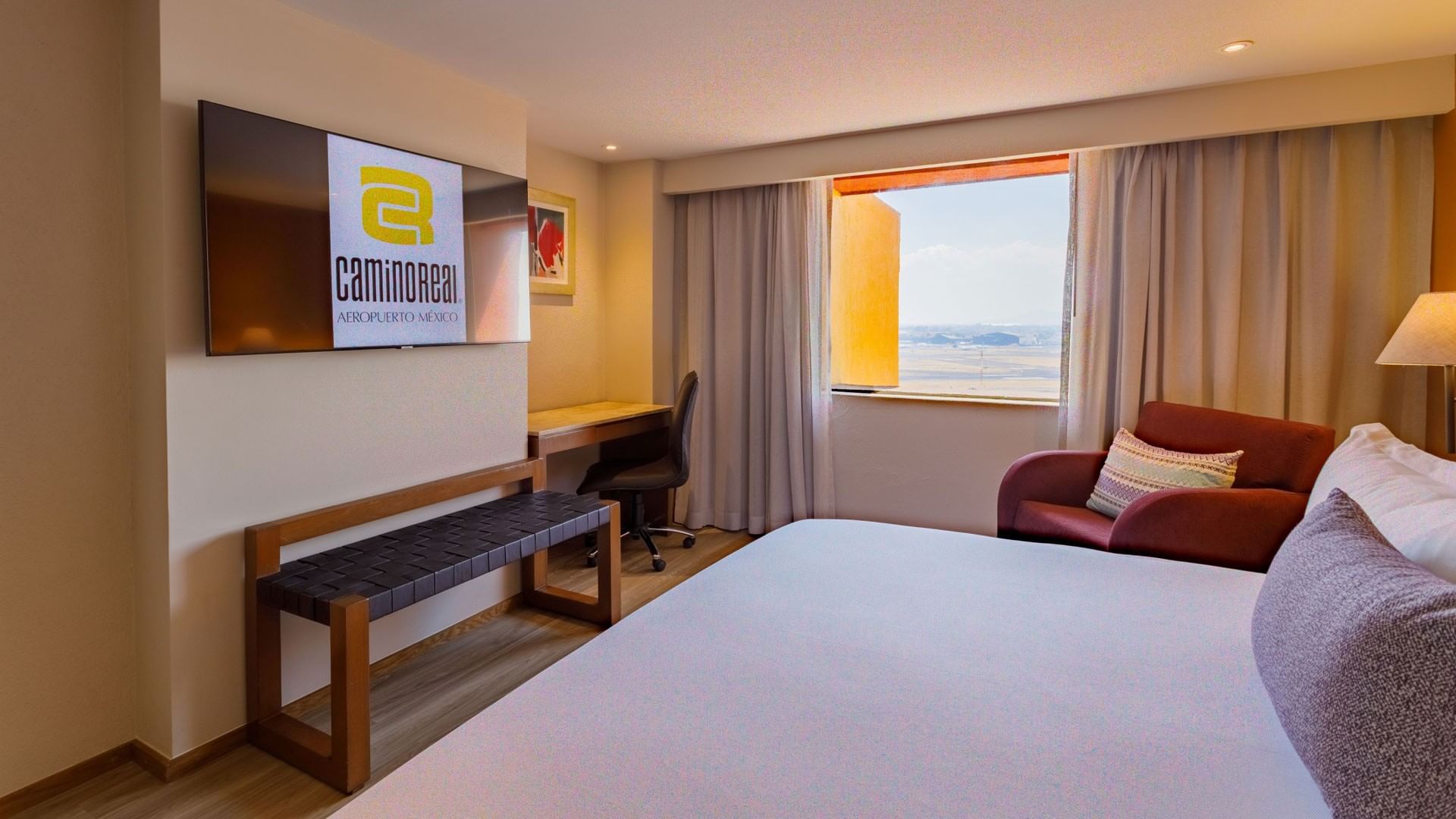 TV with wooden bench facing bed and couch by the window in  King Deluxe Superior room at Camino Real Aeropuerto Mexico