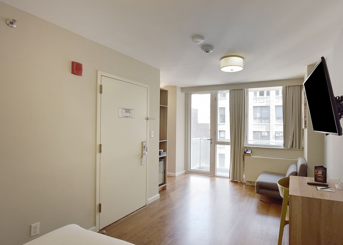A hotel room with a queen-sized bed, a TV, a desk, and a balcony